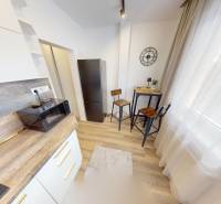 Kitchen corner with a microwave, refrigerator, and high stools in a studio apartment.