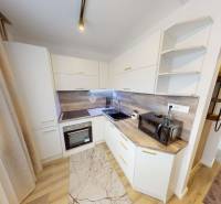 The kitchen of a one-room apartment with white cabinets, wood-patterned flooring, and appliances.