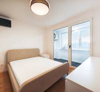 Bedroom in a two-room apartment with a bed, table, and balcony, wooden decor flooring.