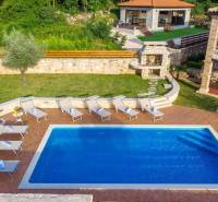 A villa in the town of Bale with a pool, sun loungers, and a stone seating area surrounded by greenery.