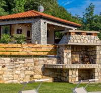 Stone facade and outdoor fireplace at the villa in Bale, surrounded by greenery and trees.