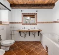 Bathroom in a villa with white walls, bathtub, sinks, and floor with wooden decor.
