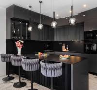 Black kitchen in a villa with marble flooring and luxurious chairs.