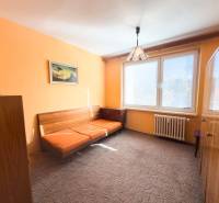 A room in a 3-room apartment with orange walls, a sofa, and a large window.
