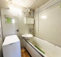 A bathroom in a 3-room apartment with a bathtub, sink, and washing machine, floor with wooden decor.