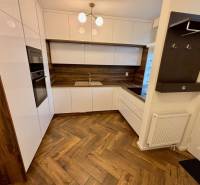 A kitchen in a 2-room apartment with a white kitchen unit and a floor with a wood decor.
