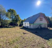 A cottage in Lackov on a sunny meadow surrounded by trees and a blue sky.