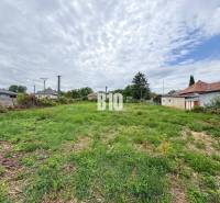 Plots for residential use in Bardoňovo, surrounded by houses and vegetation under a cloudy sky.