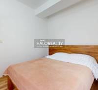 A bedroom with wooden decor, a bed, and a view of the adjacent living room in a three-room apartment.