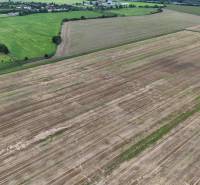 Agricultural and forest land near Nová Ves nad Váhom with a threshed field and green trees.