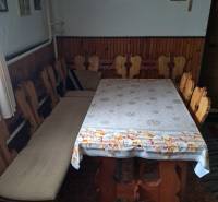 A dining room in a family house with wooden chairs and a table, the wall is adorned with paintings and a cross.