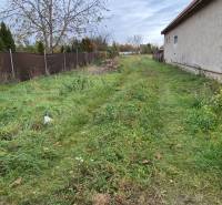 A grassy plot in Tvrdošovce designated for residential use, bordered by a fence and a building.