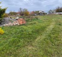 Green residential land in Tvrdošovce with piles of debris and dense vegetation.