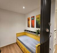 A studio apartment with a single bed, paintings of trees, and a floor with a wood decor.