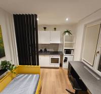 Studio apartment with a yellow bed, kitchen, table, and a wooden-patterned floor.