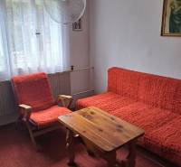 A room in a family house with red armchairs, a table, and curtain drapes.