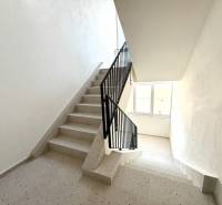 A staircase in an apartment building with a window, white walls, and tiles.