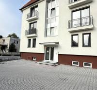 The building on Sadová Street in Senica with a white facade and a paved parking lot.