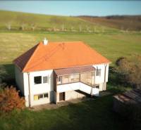 A family house in Dobrá Voda with a sloped roof, surrounded by greenery and meadows.