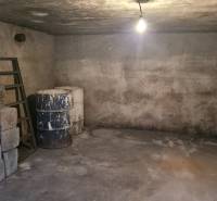 The basement of a family house with a concrete floor, you notice barrels and stairs.
