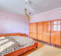Bedroom in a family house with a large bed, cabinet, and ceiling chandelier.