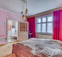 A bedroom in a family house with pink wallpaper and red curtains.