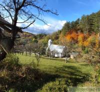 Autumn in the gardens of Hlboké nad Váhom with a small church among the trees, colorful forests in the background.