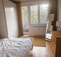 A bedroom in a 2-room apartment with a wood-patterned floor, a bed, and a mirror.