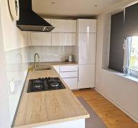 A kitchen in a 2-room apartment with white cabinets and a wooden-patterned floor.