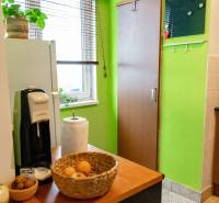 A kitchen in a 2-room apartment with wooden decor, green walls, and a window with blinds.