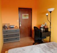 A room in a 2-room apartment with orange walls, a table, and a shelf.