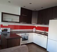 A kitchen in a 3-room apartment with white cabinets and red tiles, and a wooden decor floor.