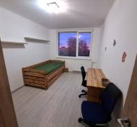 A room with a bed and a table in a 3-room apartment, with a floor featuring a wood decor.