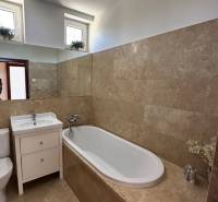 A bathroom in a family house with a bathtub, a sink, and brown tiles.