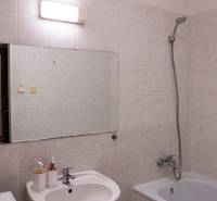 Bathroom in a 2-room apartment with a bathtub, sink, and lighting above the mirror.