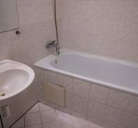 A bathroom with a bathtub, a sink, and tiles in a 2-room apartment.