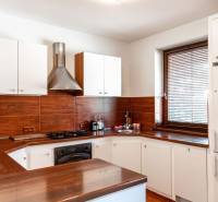 A kitchen with white cabinets, brown tiles, and a dark workspace in a two-room apartment.
