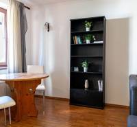 Living room with a window, table, bookshelf, two chairs, sofa, and wooden-patterned floor.