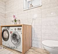 A bathroom in a 3-room apartment with a washing machine, dryer, and a floor with a wooden decor.