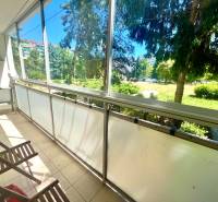 Glazed loggia with wooden chairs and a view of greenery in a 3-room apartment.