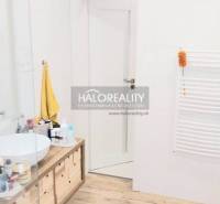 A bathroom with a wooden decor floor, a countertop sink, and white walls in a three-room apartment.