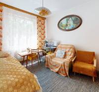 A room in a family house with a bed, carpet, armchair, and a picture on the wall.