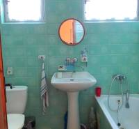 A bathroom in a family house with turquoise tiles, a sink, a mirror, and a bathtub.