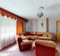 Living room in a family house with floral wallpaper, a soft sofa, and long curtains.