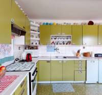 A kitchen in a family house with olive cabinets, appliances, and shelves with cups.