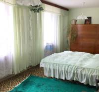 A bedroom in a family house with carpets, curtains, and a wooden wardrobe.