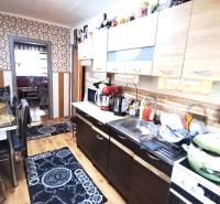 A kitchen in a 2-room apartment with a wooden decor floor and geometric wallpaper.