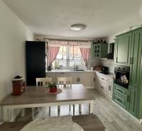 A kitchen in a family house with green cabinets, a dining table, and red curtains.