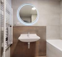 A bathroom with a sink, mirror, and bathtub in a 2-room apartment, with subtle tiles.