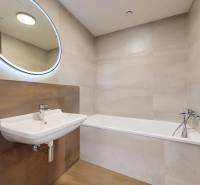 Bathroom in a 2-room apartment with a bathtub, sink, and round mirror.